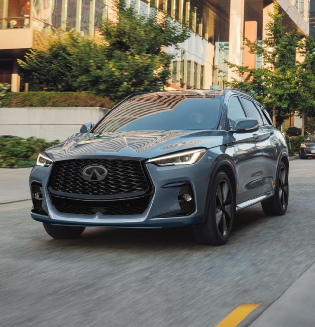 Front end of INFINITI driving through urban environment with buildings and greenery